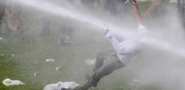 Homem recebe um jato de canhão de água durante confrontos, enquanto pessoas se reuniam em um parque em desafio às restrições belgas devido à covid-19, em Bruxelas