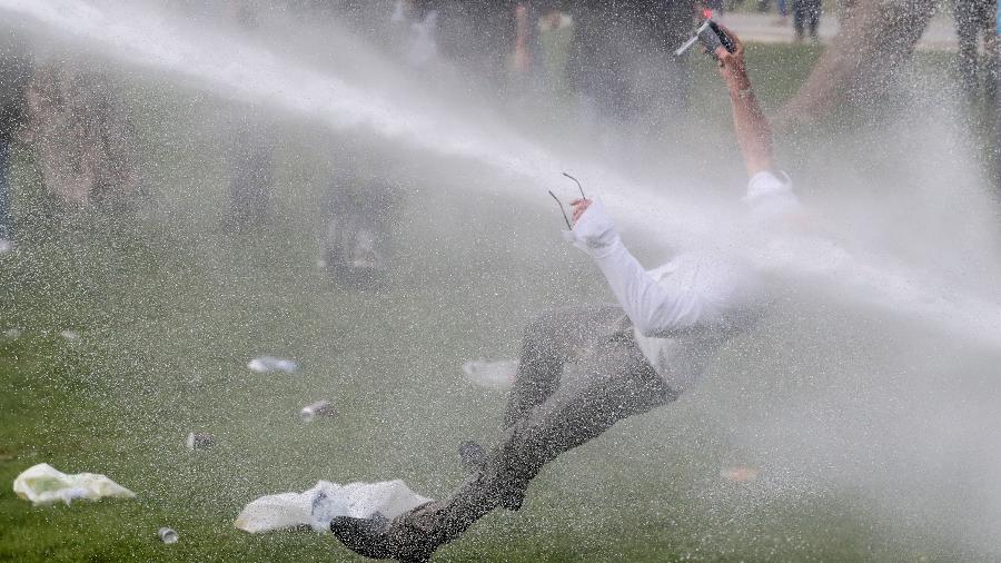 Homem recebe um jato de canhão de água durante confrontos, enquanto pessoas se reuniam em um parque em desafio às restrições belgas devido à covid-19, em Bruxelas - Yves Herman/Reuters