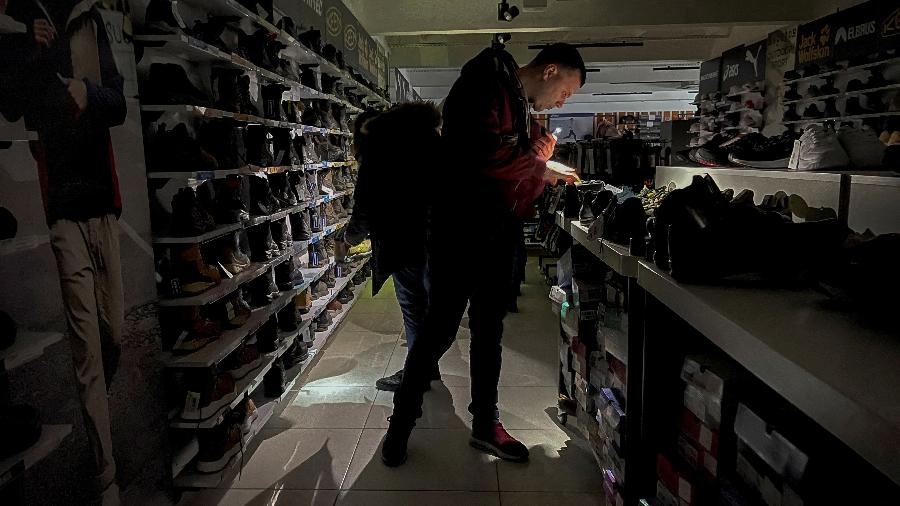 26.nov.22 - As pessoas usam as lâmpadas de seus telefones celulares para olhar itens em uma loja de artigos esportivos durante uma queda de energia - GLEB GARANICH/REUTERS