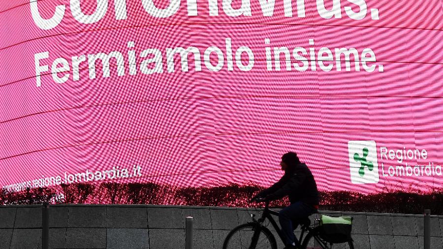 Pessoa anda de bicicleta por anúncio sobre coronavírus em Milão - FLAVIO LO SCALZO