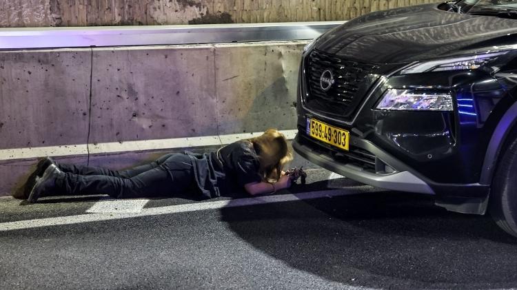 Uma pessoa se protege perto dos carros durante ataque do Irã em Tel Aviv