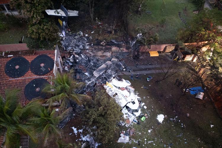 Imagem aérea mostra gramado com destroços do avião de cor branca. Ao lado direito, há o telhado de uma casa