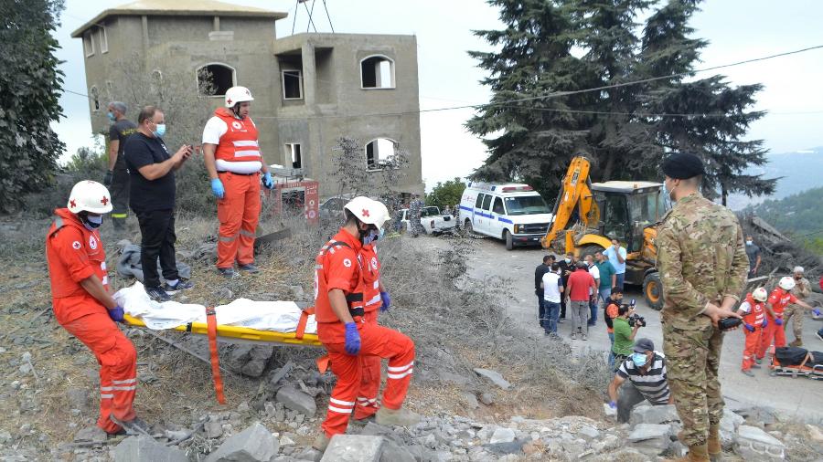 Paramédicos da Cruz Vermelha Libanesa transportam um corpo no local de um ataque aéreo israelense que atingiu a vila de Aitou, no norte do Líbano