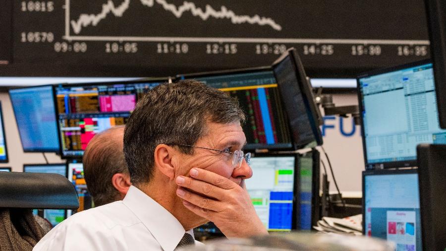 Analistas trabalham em frente a uma tla que mostra os dados da Bolsa da Alemanha, em dia de caos nos mercados financeiros - Torsten Silz/AFP