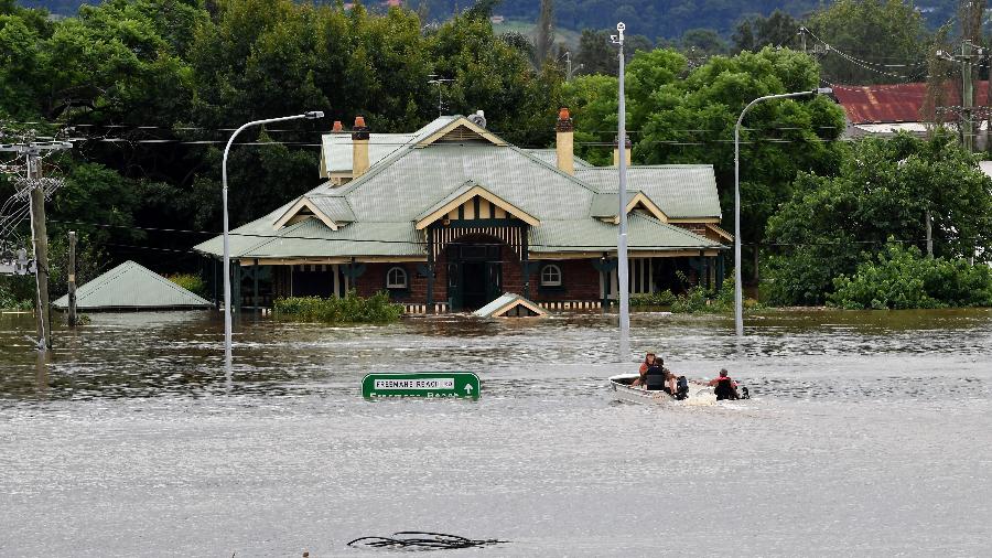 09.mar.22 - Pessoas dirigem um barco através da antiga ponte de Windsor sob as águas da enchente ao longo do rio Hawkesbury, em Sydney - SAEED KHAN/AFP