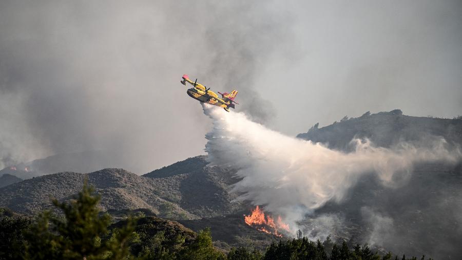 25.jul.2023 - Avião de combate a incêndio joga água sobre um incêndio florestal na ilha grega de Rodes