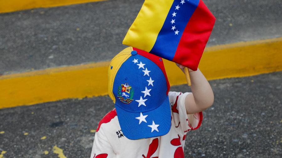 Menino segura bandeira da Venezuela durante eleição neste domingo (28), em Caracas - Enea Lebrun/REUTERS