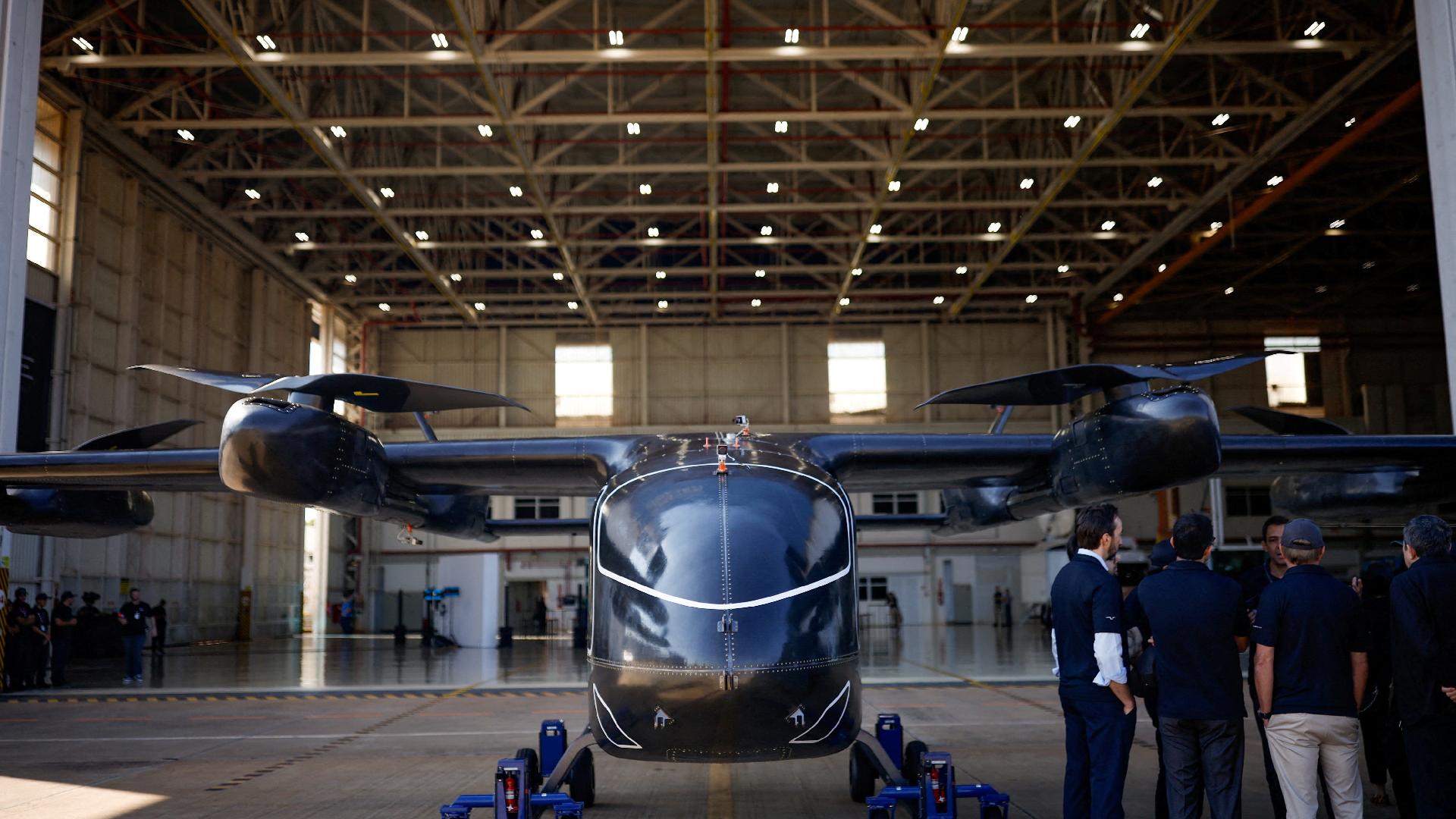 Pessoas estão ao lado do protótipo em tamanho real da aeronave elétrica de decolagem e pouso vertical (eVTOL) desenvolvida pela Eve Air Mobility, uma empresa do grupo Embraer, durante sua apresentação pela primeira vez em Gavião Peixoto, Brasil, em 3 de julho de 2024
REUTERS/Amanda Perobelli - undefined