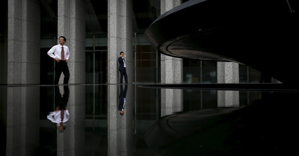 14.ago.2015 - Empresários passam por fonte em frente a um prédio de escritórios em Tóquio, no Japão