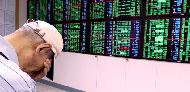 Investidor cobre o rosto em frente a painel da Bolsa de Taiwan, que caiu 4,84% hoje - David Chang/EFE