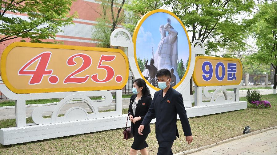 25.abr.2022 - Pessoas com máscaras passam por placa que marca o 90º aniversário de fundação do Exército Revolucionário do Povo Coreano em Pyongyang, na Coreia do Norte - Kim Won Jin/AFP
