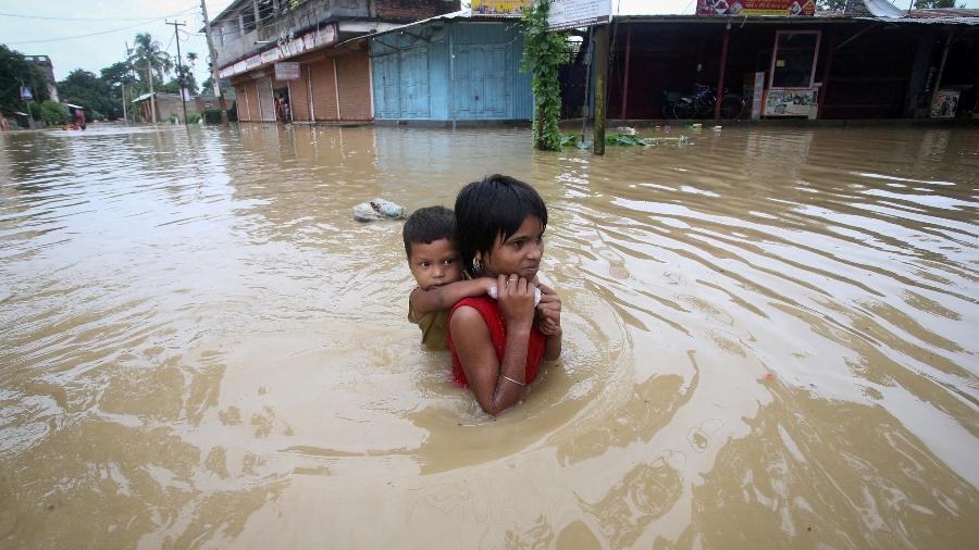 Menina carrega seu irmão enquanto caminha por estrada inundada após fortes chuvas nos arredores de Agartala, cidade da Índia - Jayanta Dey/Reuters