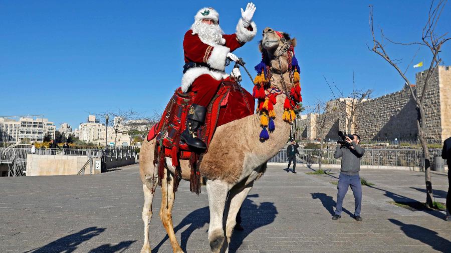 Homem vestido de Papai Noel acena para multidão montado em um camelo - Ahmad Gharabli/AFP