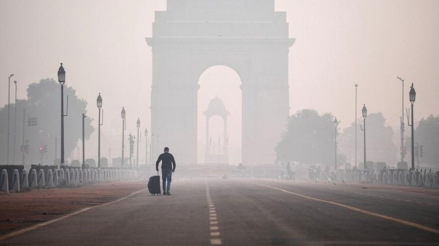 Um homem com uma mala caminha em direção ao Portão da Índia em Nova Déli envolto em poluição - Getty Images