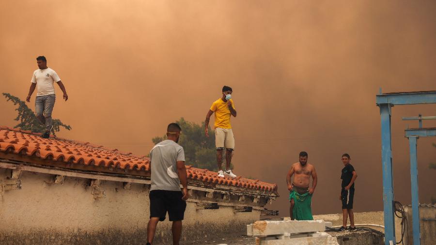 Pessoas no telhado de um prédio em meio a um incêndio florestal em Vrilissia, perto de Atenas, Grécia, 12 de agosto de 2024