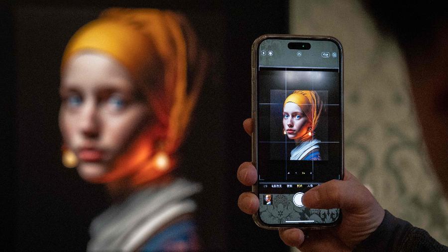 Visitante tira foto com arte feita em inteligência artificial do artista Julian van Dieken, que foi inspirda em pintura de Johannes Vermeer; artistas estão preocupados que inteligência artificial "roube" seus estilos - Simon Wohlfahrt/AFP