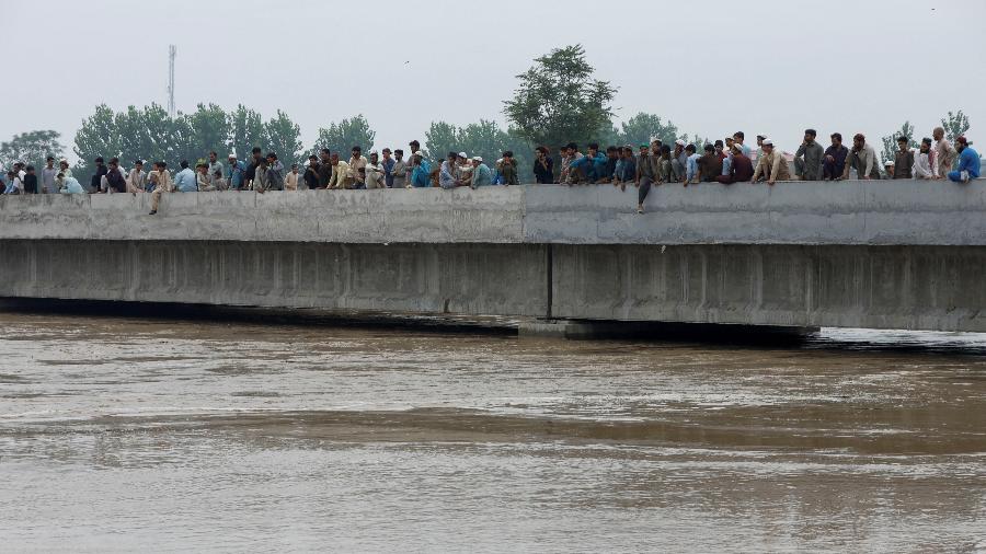 27.ago.22 - Homens se reúnem enquanto observam o fluxo das águas da enchente debaixo de uma ponte, após chuvas e inundações durante a estação das monções em Charsadda, Paquistão - FAYAZ AZIZ/REUTERS