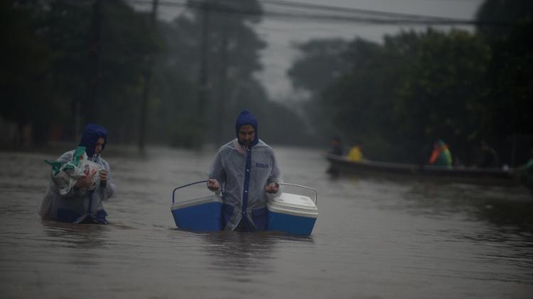 Homens carregam mantimentos em rua inundada pelas enchentes, em Eldorado do Sul (RS)