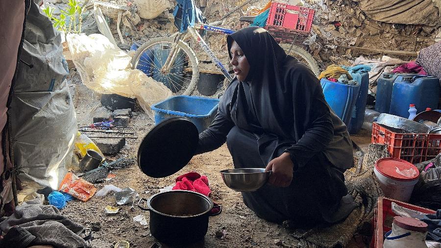 A mulher palestina Amani Maarouf senta-se com uma tigela de metal contendo macarrão em frente à sua tenda, onde se abrigou após ser deslocada, na Cidade de Gaza, em 25 de maio de 2025