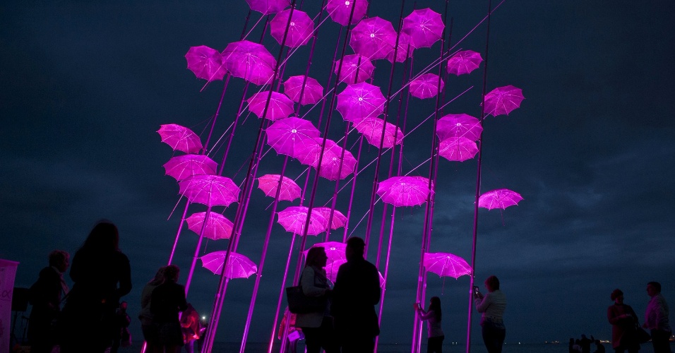 22.out.2015 - Pessoas admiram escultura com guarda-chuvas do artista Giorgos Zogopoulos iluminada de rosa para a campanha de prevenção do câncer de mama, em Thessaloki, na Grécia