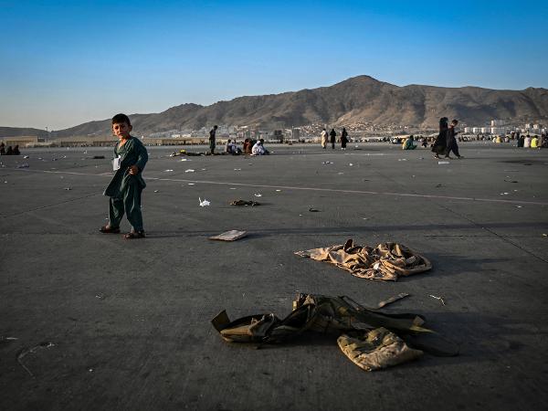 Uma criança afegã caminha entre uniformes militares enquanto aguarda para deixar Cabul no aeroporto da região - WAKIL KOHSAR/AFP