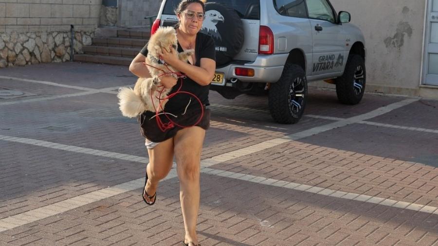 Mulher corre com cachorro na cidade de Ashkelon, no sul de Israel, após soarem alarmes de ataques vindos da Faixa de Gaza