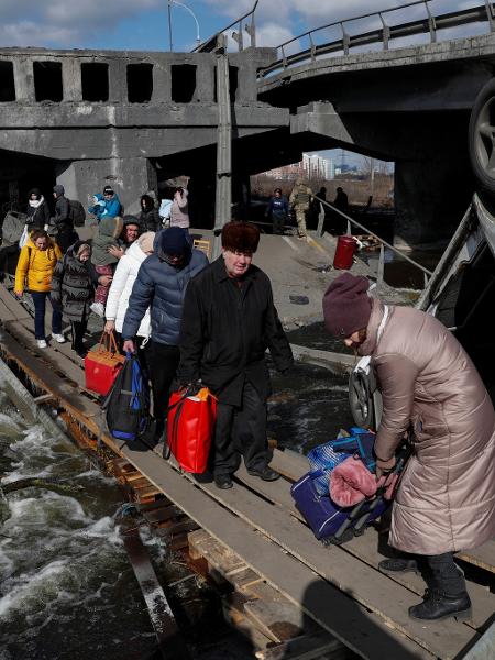 Pessoas atravessam o rio Irpin ao lado de uma ponte destruída, em meio ao ataque da Rússia à Ucrânia - VALENTYN OGIRENKO/REUTERS