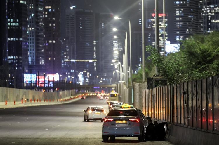 1.out.2024 - Pessoa se esconde atrás de carro enquanto Tel Aviv é atacada