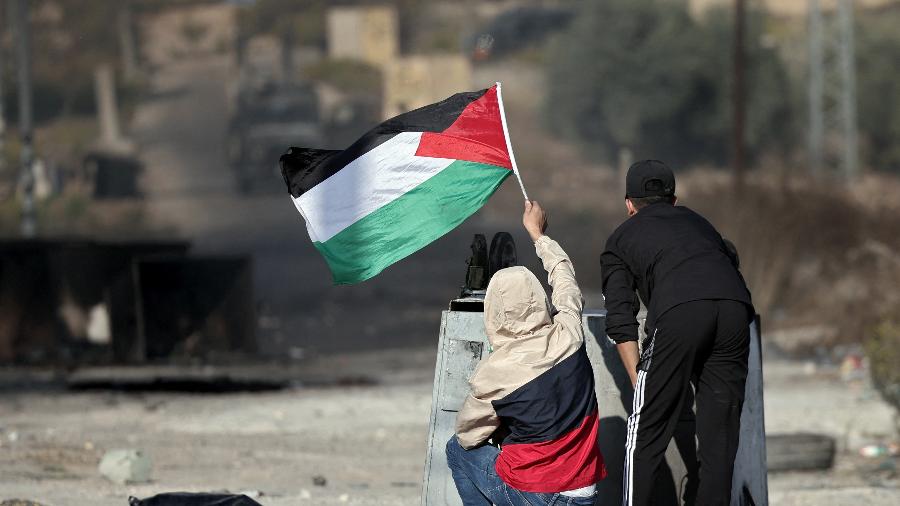 18.out.2023 - Menino agita bandeira palestina enquanto manifestantes enfrentam soldados israelenses durante um protesto em Ramallah, na Cisjordânia