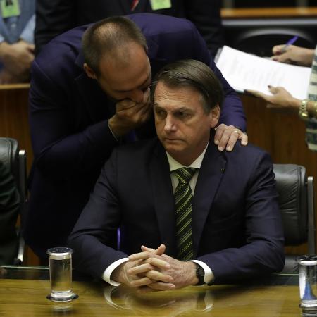 15.jul.2019 - Deputado federal Eduardo Bolsonaro (PSL-SP) sussurra no ouvido do pai, o presidente Jair Bolsonaro (PSL), durante sessão solene na Câmara - GABRIELA BILó/ESTADÃO CONTEÚDO