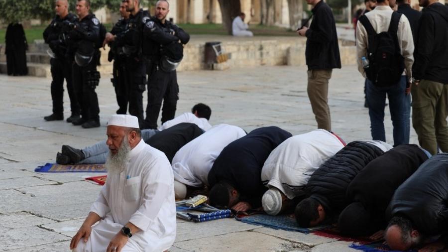 9.abr.2023 - Muçulmanos rezam próximos à mesquita de Al-Aqsa durante o mês sagrado do Ramadã; ao fundo, militares israelenses acompanham a movimentação