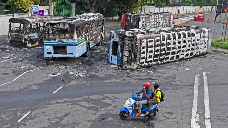 Na imagem: homens em uma moto passam perto de ônibus queimados nas proximidades da residência oficial do hoje ex-primeiro-ministro - Ishara S. Kodikara/AFP