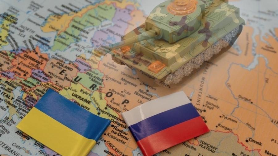 Bandeiras da Ucrânia e da Rússia, próximas a um carro-tanque de brinquedo, sobre um mapa da Europa - Brasil Escola