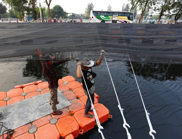 Trabalhadores usam rede para cobrir um rio poluído em Jacarta, na Indonésia - Willy Kurniawan/Reuters