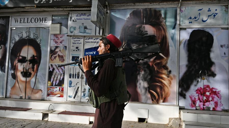Membro do Talibã passa em frente a um salão de beleza em Cabul, que teve imagens de mulheres na fachada vandalizadas - Walki Kohsar/AFP