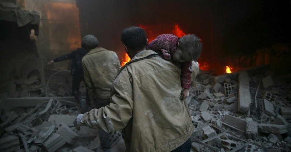 30.dez.2015 - Homem carrega criança ferida de local destruído por um ataque a bomba de forças leais ao presidente sírio, Bashar al-Assad, na cidade de Douma, no leste de Ghouta, em Damasco, Síria