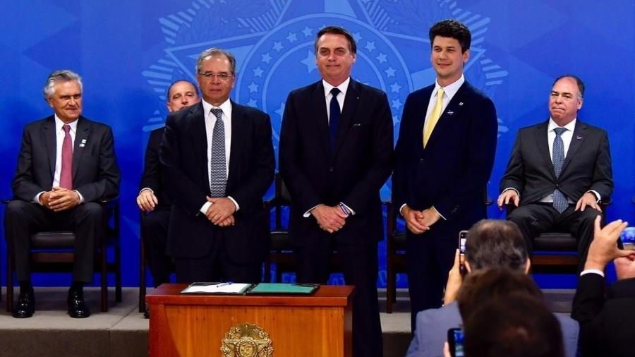 Gustavo Montezano (em pé, à dir.) toma posse como novo presidente do BNDES, ao lado do presidente Jair Bolsonaro (centro) e do ministro da Economia, Paulo Guedes (em pé, à esq.) - Divulgação/BNDES
