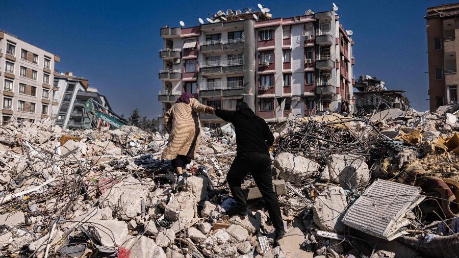 Casal escala os escombros de prédios desabados em Antakya, sul da Turquia, nesta segunda (20) - Sameer Al-Doumy/AFP
