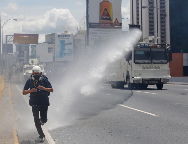 Jornalista corre de jato d"água lançado por carro das forças de segurança durante protesto contra o governo de Nicolás Maduro, em Caracas - Ivan Alvarado/ Reuters