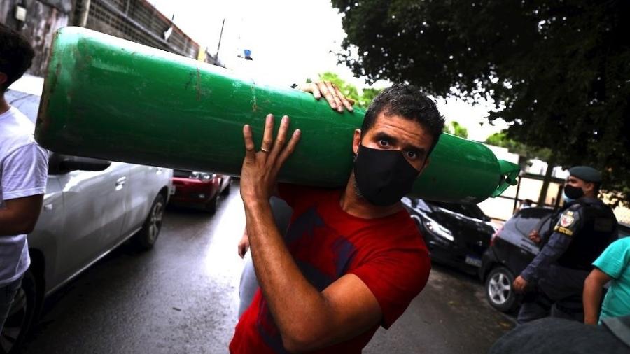 Um homem carrega um cilindro de oxigênio enquanto pessoas fazem fila para comprá-lo de vendedores particulares para tratar de parentes doentes em Manaus, 15 de janeiro de 2021 - Reuters