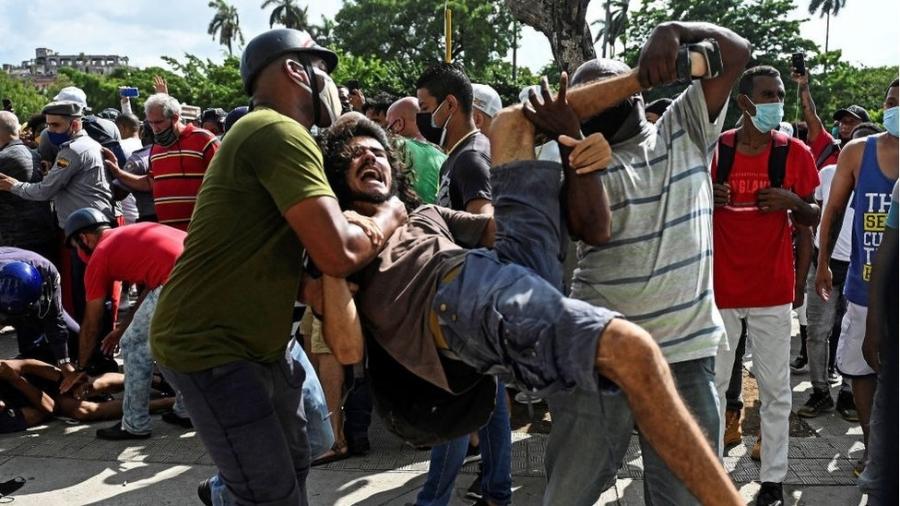 Manifestante sendo carregado durante protesto em Cuba neste domingo - AFP
