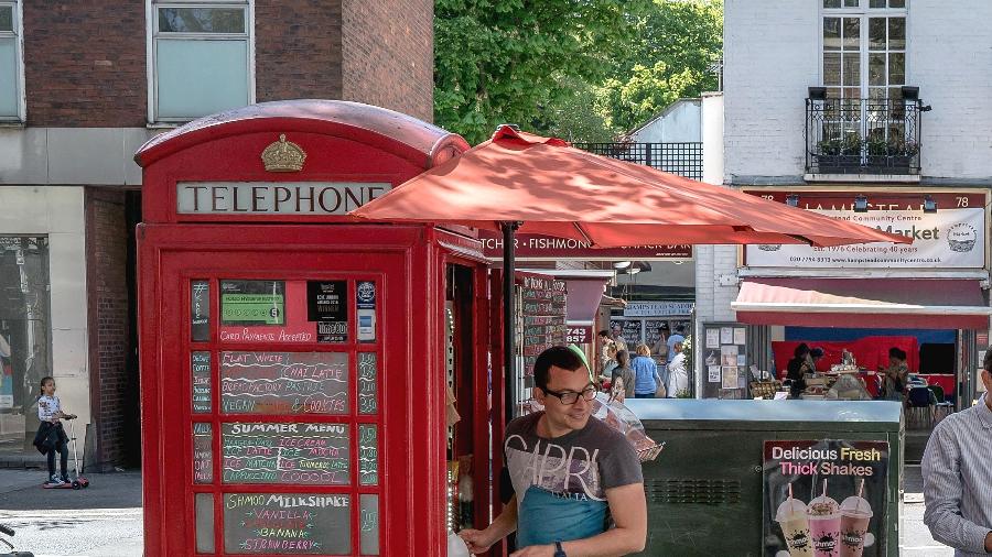 Homem serve café e bolos em uma cabine telefônica transformada em um café em Londres - Andrew Testa/The New York Times