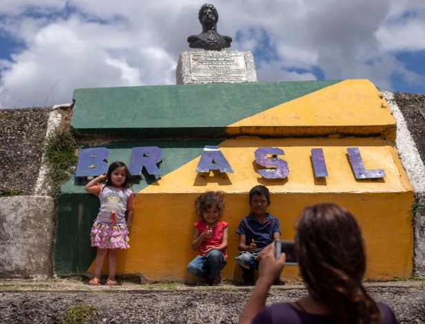 Crianças venezuelanas tiram foto em frente a monumento na fronteira Brasil - Venezuela, em Roraima - Mauro PIMENTEL / AFP