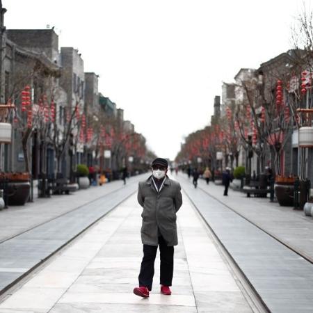 Homem caminha de máscara por rua deserta de Pequim - THOMAS PETER