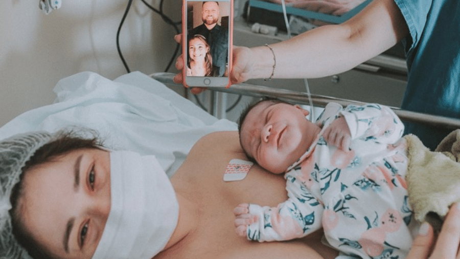 Mayara com a recém-nascida no colo e o celular com uma foto do pai e da irmã, Isabelly - Reprodução/Instagram/@benditoventrefotografia