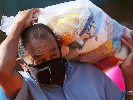 Homem carrega cesta básica distribuída pelo G10 das Favelas" em Heliópolis, São Paulo - CARLA CARNIEL/REUTERS
