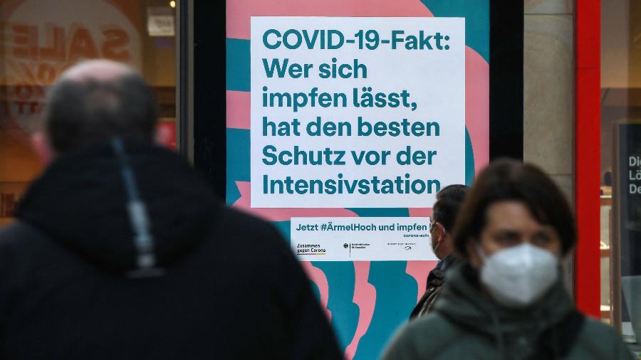Pessoas caminham em rua de Dortmund, na Alemanha, onde há uma placa que diz que quem se vacina tem a melhor proteção contra internação por casos graves de covid-19 - 13.jan.2022 - Ina Fassbender/AFP