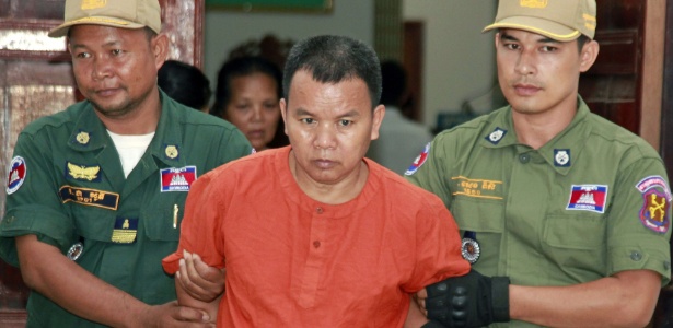O médico Yem Chroeum (centro) é conduzido por policiais durante julgamento na província de Battambang, no Camboja - AFP