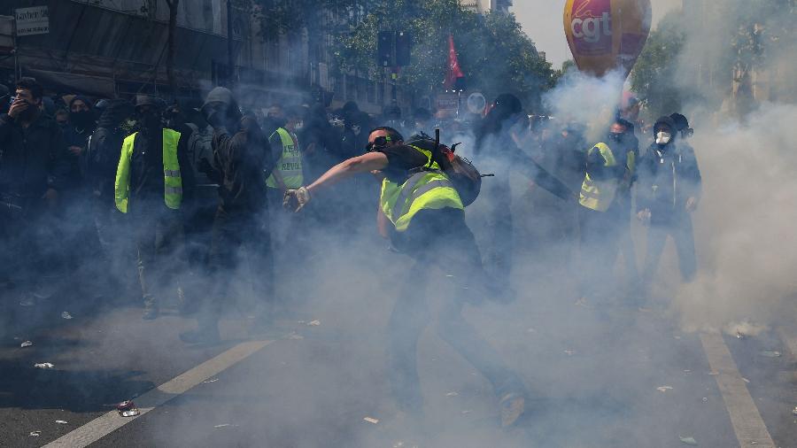 1º.mai.2019 - Manifestantes mascarados vestidos com coletes amarelos lançam objetos contra a polícia em meio a fumaça das bombas de gás lacrimogêneo lançadas contra eles - Alain Jocard/AFP