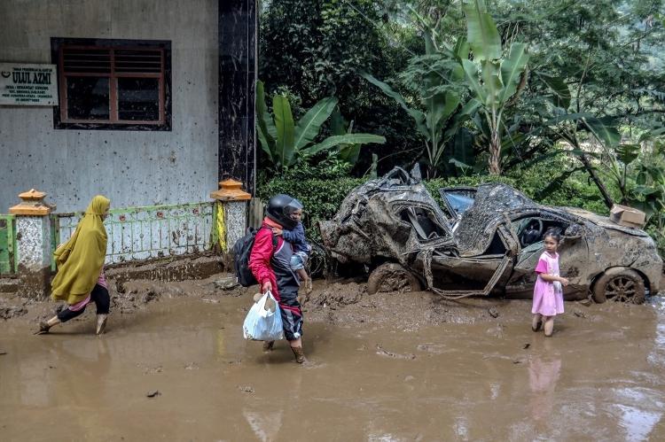 Uma família caminha pela lama, passando por um carro amassado após deslizamentos de terra na vila de Semangat Gunung em Karo, Sumatra do Norte